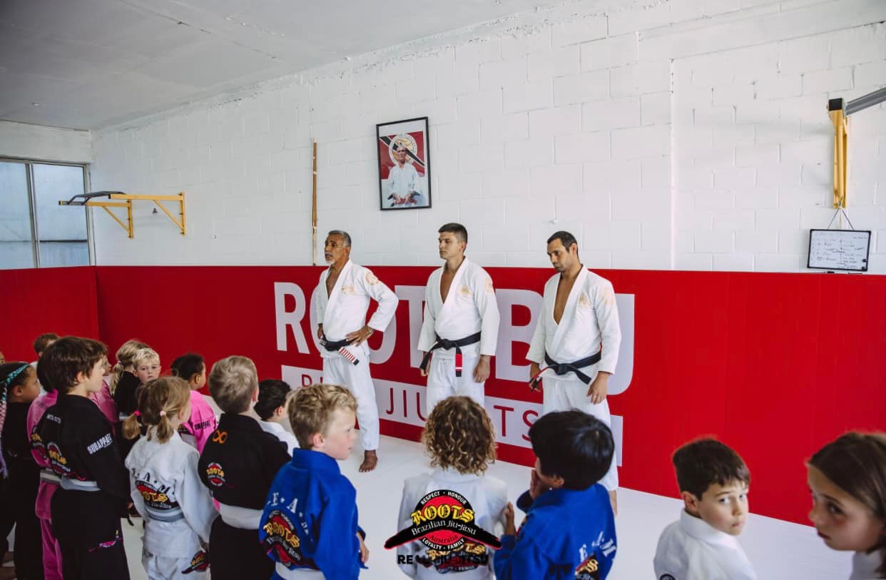 ROOTS black belt professors on the mat in front of the red academy wall